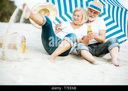 Felice coppia senior divertirsi giocando con la sabbia sulla spiaggia, godendo della loro pensione vicino al mare Foto Stock