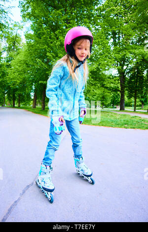 Grazioso fanciullo girl learning per pattino a rotelle sulla bellissima giornata estiva in un parco. Il bambino che indossa il casco di sicurezza godendo di pattinaggio corsa all'aperto Foto Stock