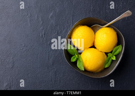 Gelato al mango tropicale sorbetto di frutta in vaso nero su sfondo di ardesia. Copia dello spazio. Vista dall'alto. Foto Stock