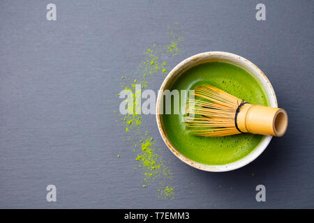 Tè verde Matcha il processo di cottura in una ciotola con una frusta di bambù. Nero ardesia sfondo. Vista dall'alto. Copia dello spazio. Foto Stock