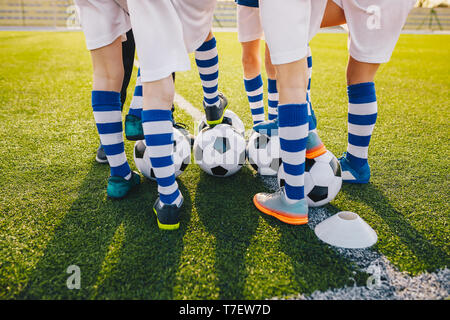 Un gruppo di giovani giocatori di calcio in allenamento per il calcio. Gambe di soccer kids calci sfere sul campo. Estate tramonto in background. Allenamento di calcio bac