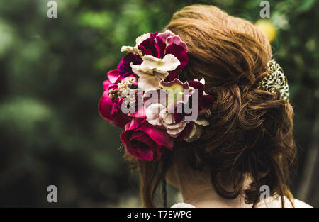 Acconciatura con fiori colorati. Capelli belli decorata con fiori. Isolato su sfondo verde. Cura dei capelli concetto. Vista dal retro Foto Stock