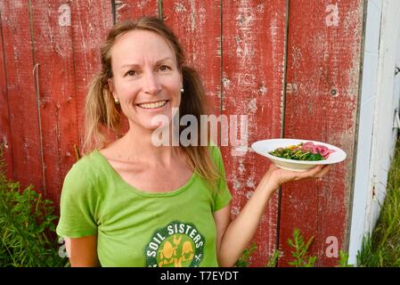 Donna agricoltore chef catering sul lavoro del suo allevamento di suini, con un pasto preparato realizzato con il patrimonio di suini che ha sollevato, Farm Cena, Blanchardville, WI, Stati Uniti d'America Foto Stock
