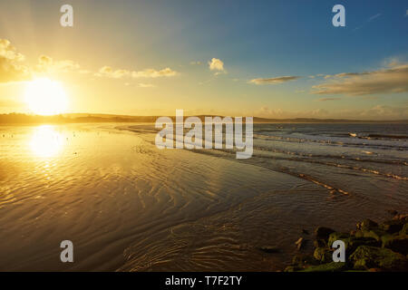 Bel tramonto sulla spiaggia con acqua riflessioni, gabbiani sulla sabbia e mulini a vento in background in Marocco con il fuoco selettivo Foto Stock