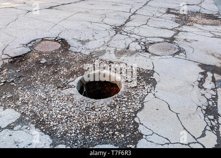 Aprire non protetta tombino fognario sulla strada asfaltata. Pit pericolose su strada. Vecchio di fognature ben berlina su strada Foto Stock