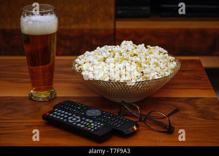 La pinta di birra ciotola di popcorn controller remoto e bicchieri su sfondo di legno intrattenimento casalinghi Foto Stock