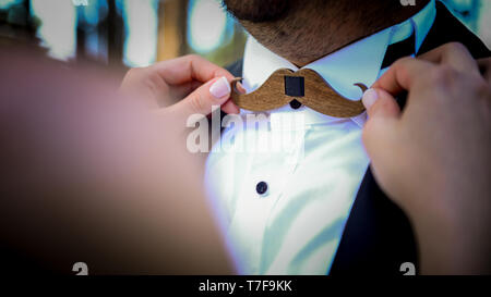 Spose in mano sull'baffi di legno a forma di papillon del groom vista ravvicinata Foto Stock