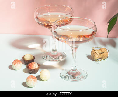 Champagne o vino in eleganti occhiali vari praline di cioccolato bianco su uno sfondo rosa hard light. Copia dello spazio. Foto Stock