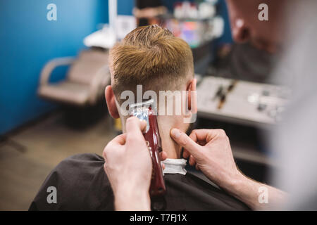 Immagine ravvicinata di un uomo di ottenere un taglio di capelli alla moda in un salone di parrucchiere. Maschio parrucchiere caucasici che serve un client. Con barba rendendo taglio di capelli con un t Foto Stock