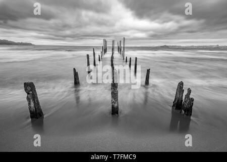 Come una strada per l'inferno un molo vecchio all'interno del lago di acque sotto un drammatico cielo nuvoloso e venti alti. I vecchi pali in legno ancora lotta contro il tempo Foto Stock