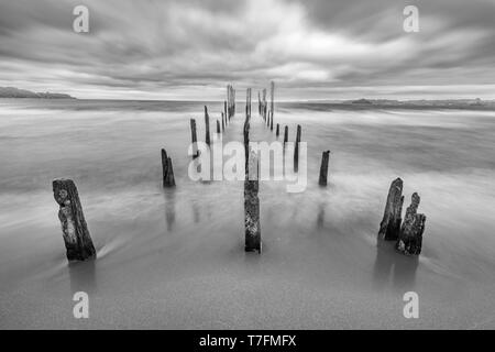 Come una strada per l'inferno un molo vecchio all'interno del lago di acque sotto un drammatico cielo nuvoloso e venti alti. I vecchi pali in legno ancora lotta contro il tempo Foto Stock