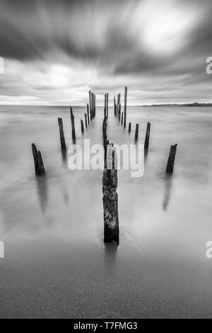 Come una strada per l'inferno un molo vecchio all'interno del lago di acque sotto un drammatico cielo nuvoloso e venti alti. I vecchi pali in legno ancora lotta contro il tempo Foto Stock