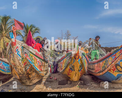 Nianing, Senegal - Gennaio 2, 2019: i pescatori la raccolta di pesce di legno colorato barca fisher permanente sulla spiaggia. Africa Foto Stock