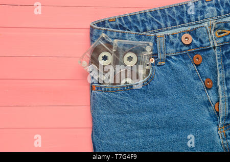 Due cassette audio in una tasca dei jeans su una rosa di superficie di legno. La tecnologia multimediale dal 80s. Foto Stock