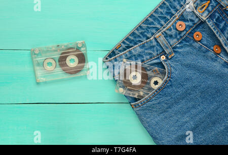 Due cassette audio in una tasca dei jeans su un blu superficie di legno. La tecnologia multimediale dal 80s. Foto Stock