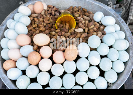 Close-up di arachidi cotti al vapore e bianco e marrone di uova sode, tutti ben presentata in una ciotola di metallo con una coppa di misurazione, per la vendita in strada Foto Stock