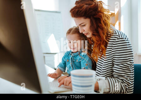 Figlia seduto sulle ginocchia della madre e cercando utilizzando la tastiera Foto Stock