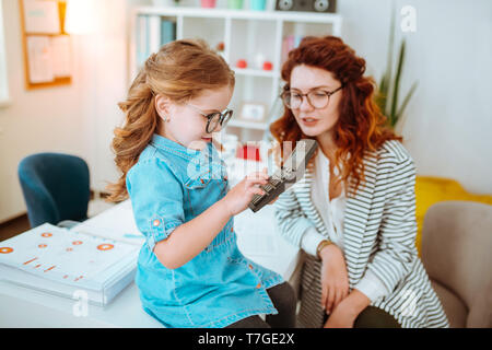 Ragazza carina denim da indossare abbigliamento e occhiali di protezione utilizzando la calcolatrice seduto vicino a MOM Foto Stock