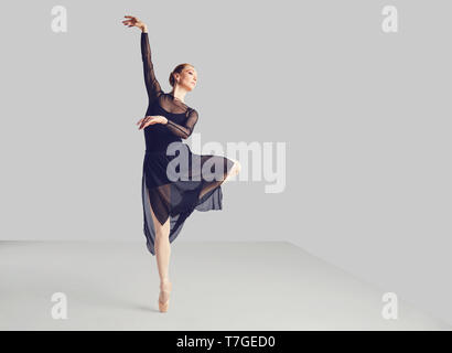 Ballerina in un nero tutu elegantemente danza su uno sfondo nero. Foto Stock