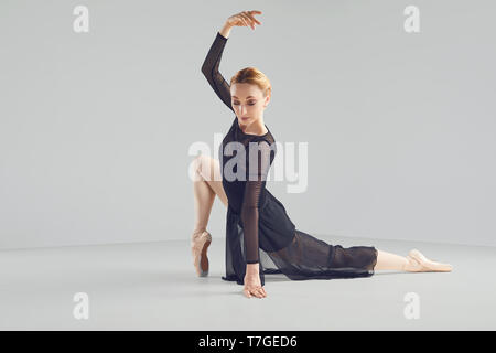 Ballerina in un nero tutu elegantemente danza su uno sfondo nero. Foto Stock