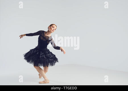 Ballerina in un nero tutu elegantemente danza su uno sfondo nero. Foto Stock