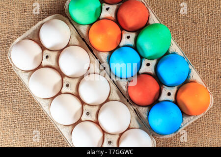 Bianche e colorate uova di pasqua in scatole di uova su un letto di sacco. Foto Stock