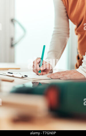 Lavoratori autonomi falegname femmina la scrittura di note del progetto su appunti notepad carta in small business workshop di falegnameria Foto Stock