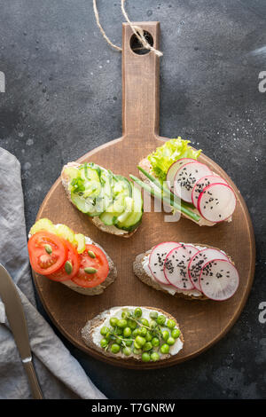 Vegano diversi panini con verdure, Rafano, sedano, pomodoro, pane di segale su sfondo nero. Top vew. Antipasto di partito. Lay piatto. Foto Stock