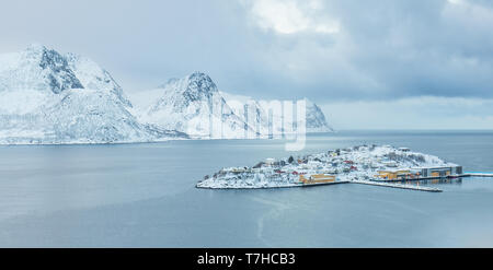 Inverno a Husoy. Piccolo borgo situato a distanti islnad settentrionale. In Sfondo coperto sonw montagne che sorgono dal mare Foto Stock