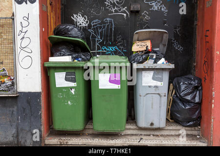 Bidoni per rifiuti pieni e traboccanti provenienti dai locali commerciali in attesa di essere svuotati in una strada cittadina, Glasgow, Scozia, Regno Unito Foto Stock