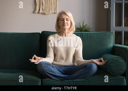 Capelli grigi donna matura meditando, a praticare yoga a casa Foto Stock