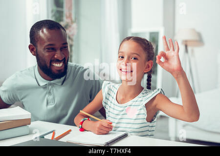 Felice ragazza che mostra il segno ok mentre papà seduto vicino a. Foto Stock