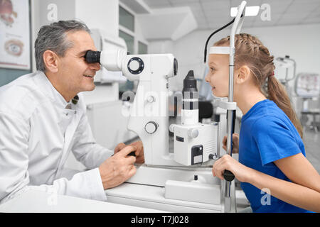 Professional medico oculista esaminando gli occhi di pretty paziente con lampada a fessura. Oculista in bianco cappotto medico guardando attraverso attrezzature speciali. Concetto di una sana visione. Foto Stock