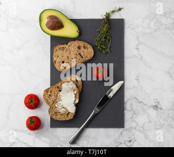 Realizzazione di una sana panini con la crema di formaggio di avocado, i pomodori e il timo. Foto Stock