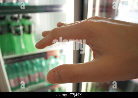 L uomo assetato si afferra con la mano per una bevanda fresca in frigorifero. Sete,ondata di calore e il concetto di sport. Foto Stock