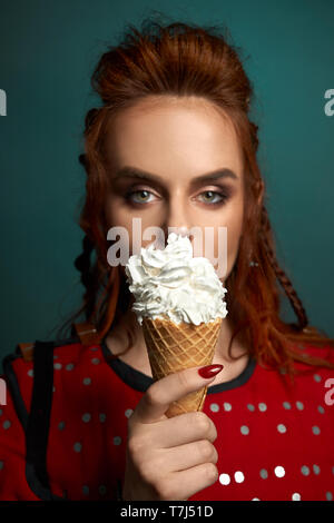 Close up di gustoso, deliziosi, bianco ice cream. Incantevole, bella donna gorgeous con zenzero capelli, pelle perfetta e make up, azienda gelato in mano, guardando la fotocamera. Foto Stock