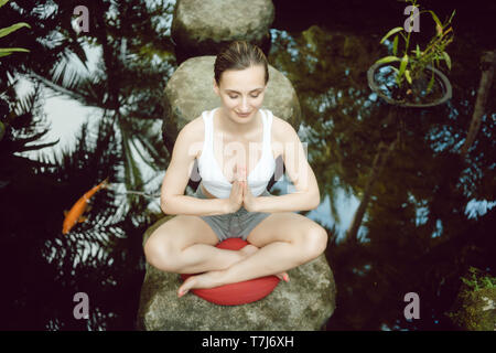 Donna fare yoga a un laghetto con pesci rossi Foto Stock