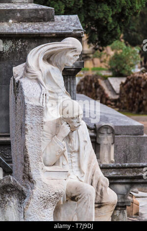 La statua di uomo e Grim Reaper sullo sfondo della tomba del cimitero di Montjuic closeup, Barcellona, in Catalogna, Spagna Foto Stock