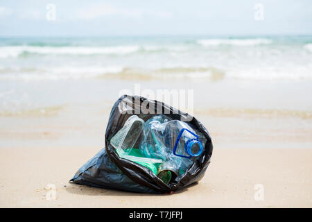 Vista dettagliata del grigio di un sacchetto di plastica con rifiuti raccolti sulla sabbia di una spiaggia solitaria, accanto all'acqua, in background Foto Stock