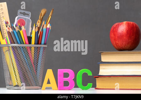 Un insieme di forniture scolastiche. Una pila di libri di testo, un apple, lettere dell'alfabeto A, B, C, matite, pennelli, vernici contro una lavagna. Il co Foto Stock