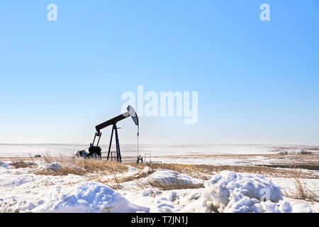 Una pompa olio del jack in un campo agricolo in inverno il paesaggio della prateria Foto Stock