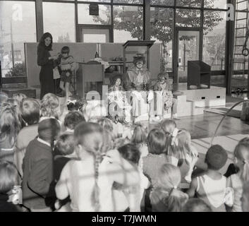 Anni sessanta, storico, un circo clown seduto su un palco in una scuola hall con due giovani scuola bambini vestiti e con le loro facce dipinte come clown, Inghilterra, Regno Unito. Foto Stock