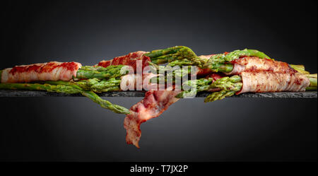 Asparagi con pancetta. Asparago Verde avvolto in pancetta su uno sfondo nero. Copia dello spazio. Foto Stock