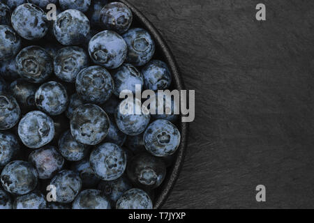 I mirtilli in tondo e nero ghisa ciotola sulla pietra nera con uno sfondo con spazio di copia Foto Stock
