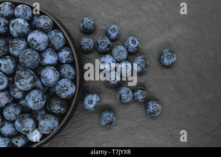 I mirtilli in tondo e nero ghisa ciotola sulla pietra nera con uno sfondo con spazio di copia Foto Stock