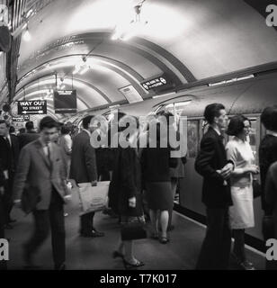 Anni sessanta, storico, all'interno di London Underground, immagine mostra un Piccadilly della metropolitana fino a una piattaforma in corrispondenza di una stazione, sulla trafficata piattaforma sono persone di salire a bordo del treno che sta per Uxbridge.... Aperto nel 1906, la linea di Piccadilly line corre da nord a Londra a nord-ovest di Londra. Foto Stock