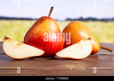 Gruppo di due interi due fette di rosso fresco pera verde con campo di grano Foto Stock