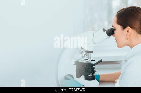 Scienziato guardando attraverso il microscopio e concentrato. La ricerca biologica Foto Stock