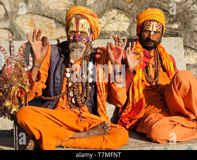 Due sadhus (uomini santi) con facce dipinte, rivestiti in arancione vesti, seduti su una panchina a Pashupatinath tempio indù, Valle di Kathmandu, Nepal Foto Stock