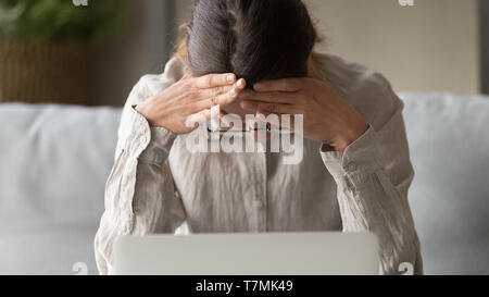 Closeup donna seduta vicino al computer portatile si sente sollecitata avente grandi problemi Foto Stock